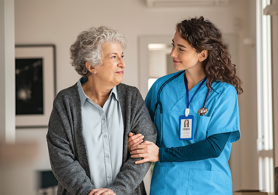 young female nurse walks arm in arm with senior citizen