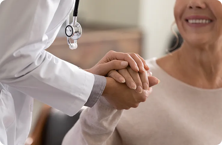 A doctor in a white coat holds the hand of a smiling patient, conveying care and reassurance.